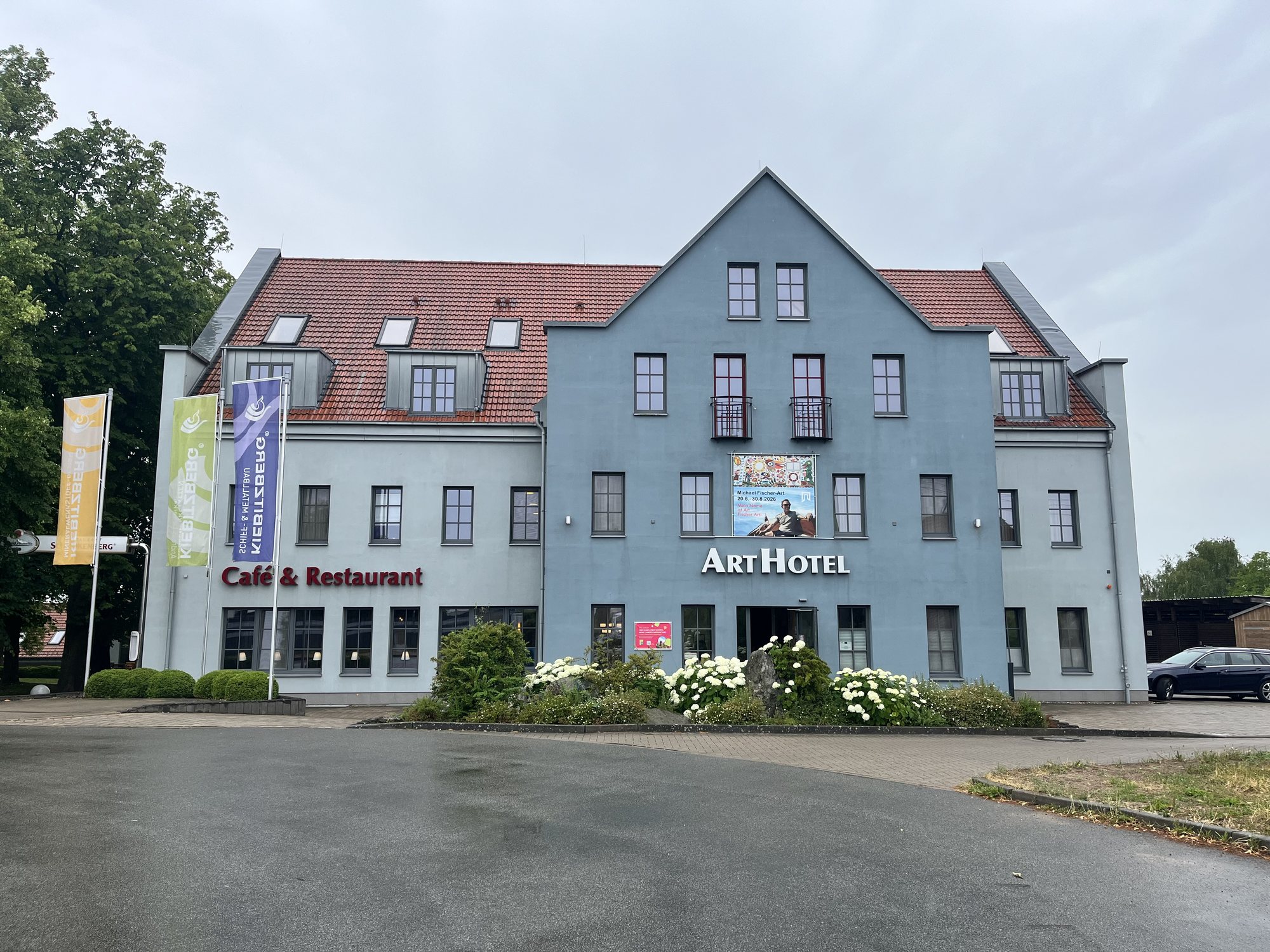 Fassade des ArtHotel Kiebitzberg mit Schriftzug ArtHotel und Café & Restaurant, Kiebitzberg-Fahnen davor