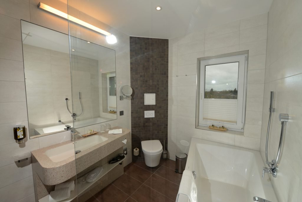 Helles Suite-Badezimmer im ArtHotel Kiebitzberg mit Badewanne, ebenerdiger Dusche, großem Spiegel und Fenster