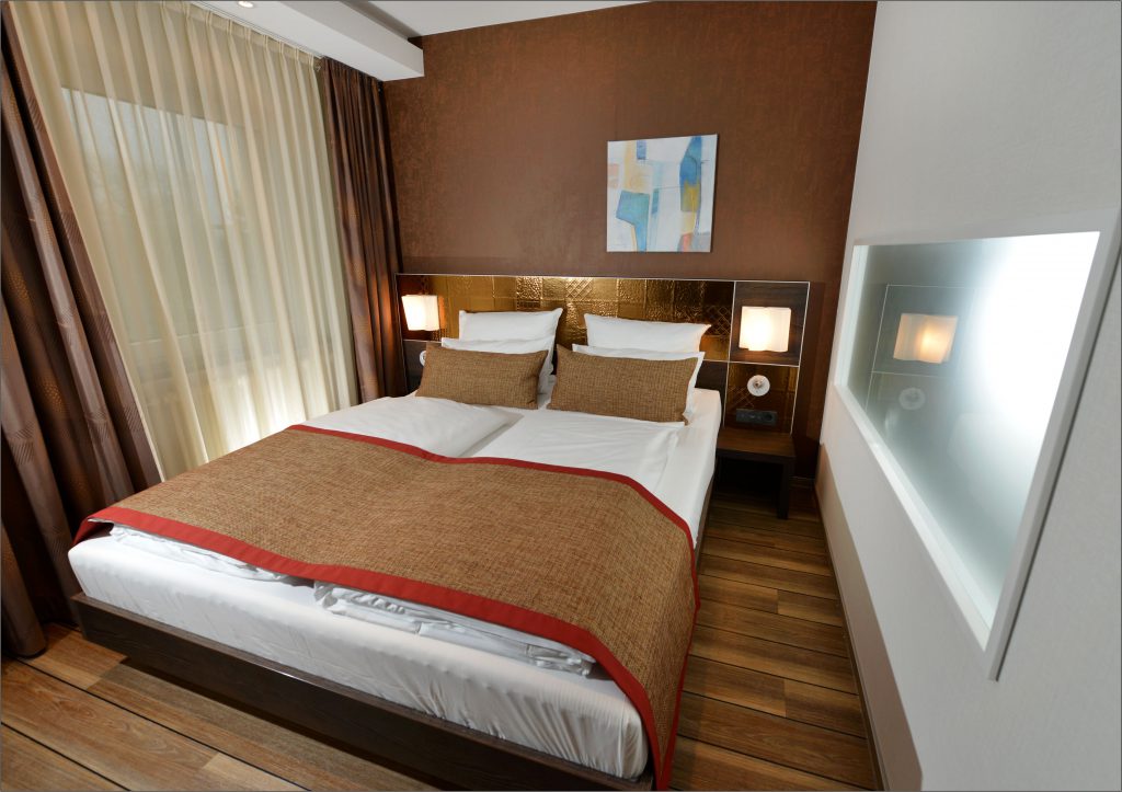 Schlafzimmer einer Suite im ArtHotel Kiebitzberg mit Doppelbett, goldenem Kopfteil und moderner Kunst