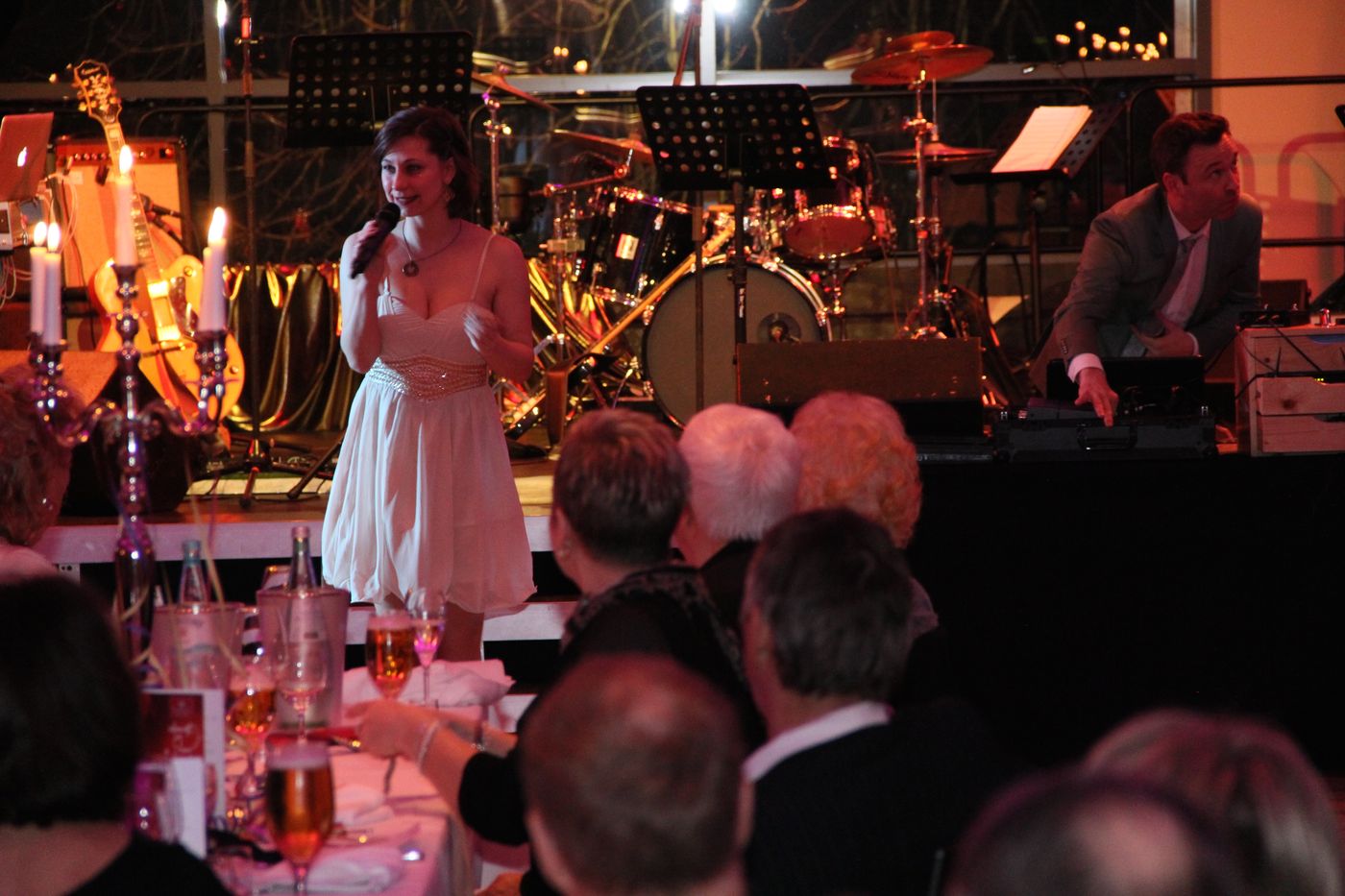 Singer in a light dress with a microphone on stage before a live band and audience at the New Year’s Eve gala at ArtHotel Kiebitzberg
