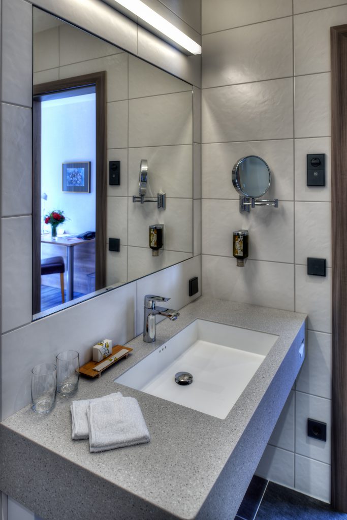 Helles Badezimmer eines Comfort-Zimmers im ArtHotel Kiebitzberg mit Waschtisch, großem Spiegel und Kosmetikspiegel