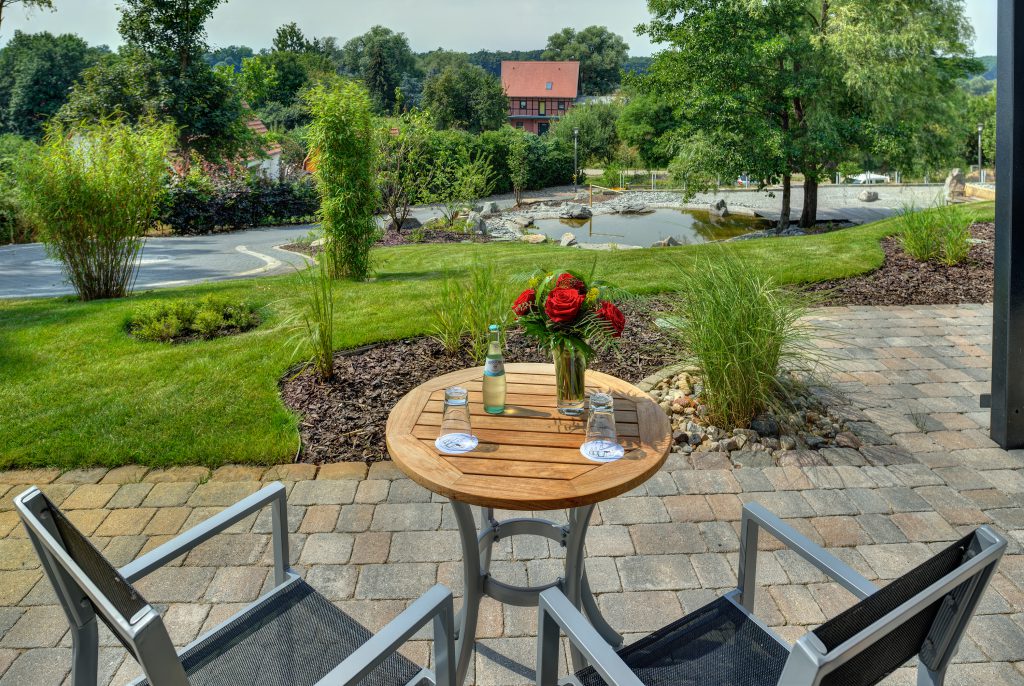 Terrasse eines Comfort-Zimmers mit Holztisch, Stühlen und Blumenstrauß, Blick auf Gartenteich und Parkanlage des ArtHotel Kiebitzberg