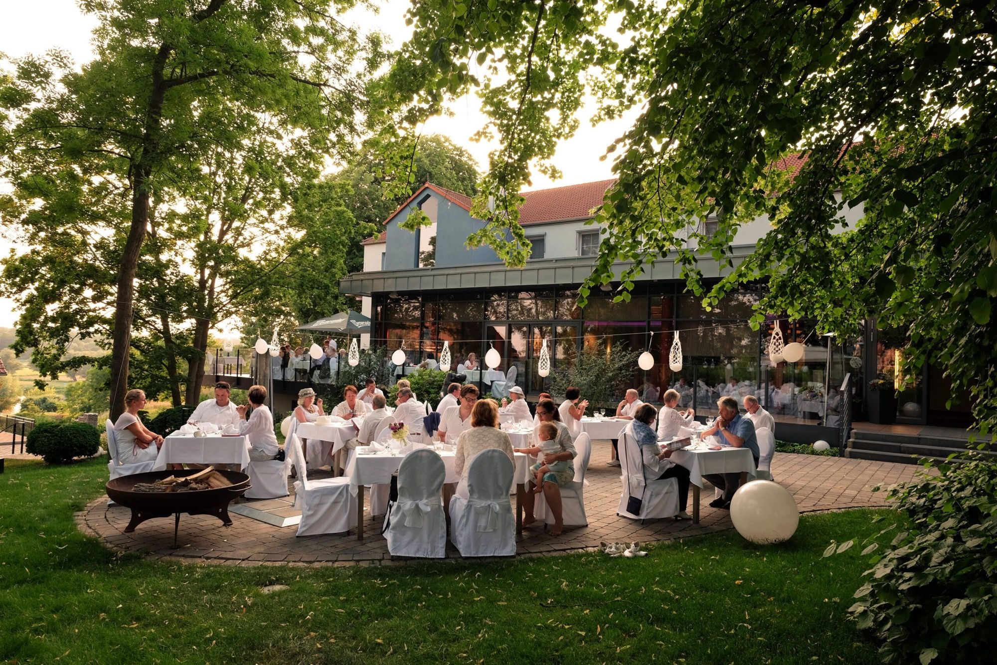 Festlich weiß gedeckte Tafel mit Gästen in Weiß im abendlichen Garten des ArtHotel Kiebitzberg