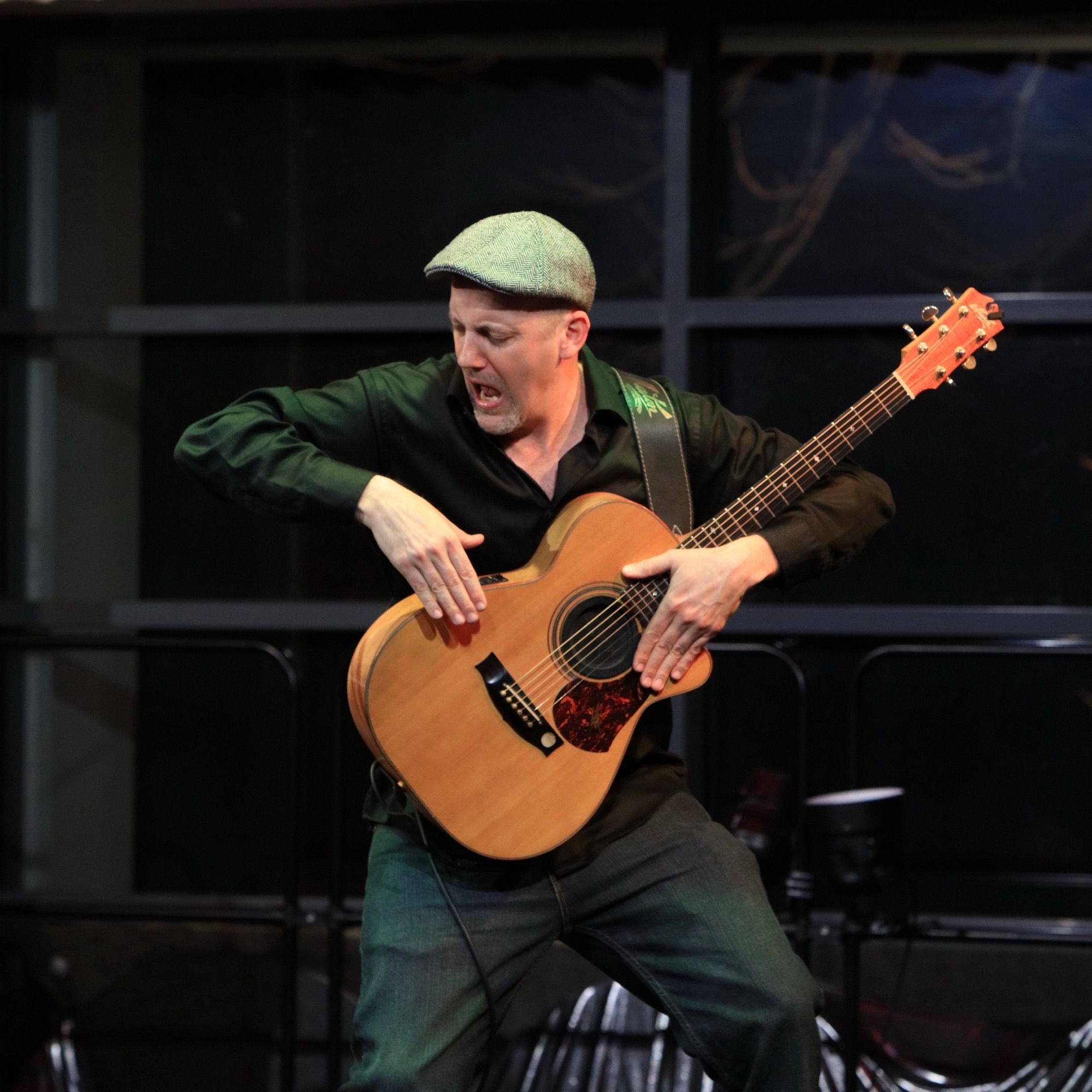 Gitarrist mit grüner Schiebermütze spielt energiegeladen Akustikgitarre auf der Bühne – Kiebitzberg in Concert im ArtHotel Kiebitzberg