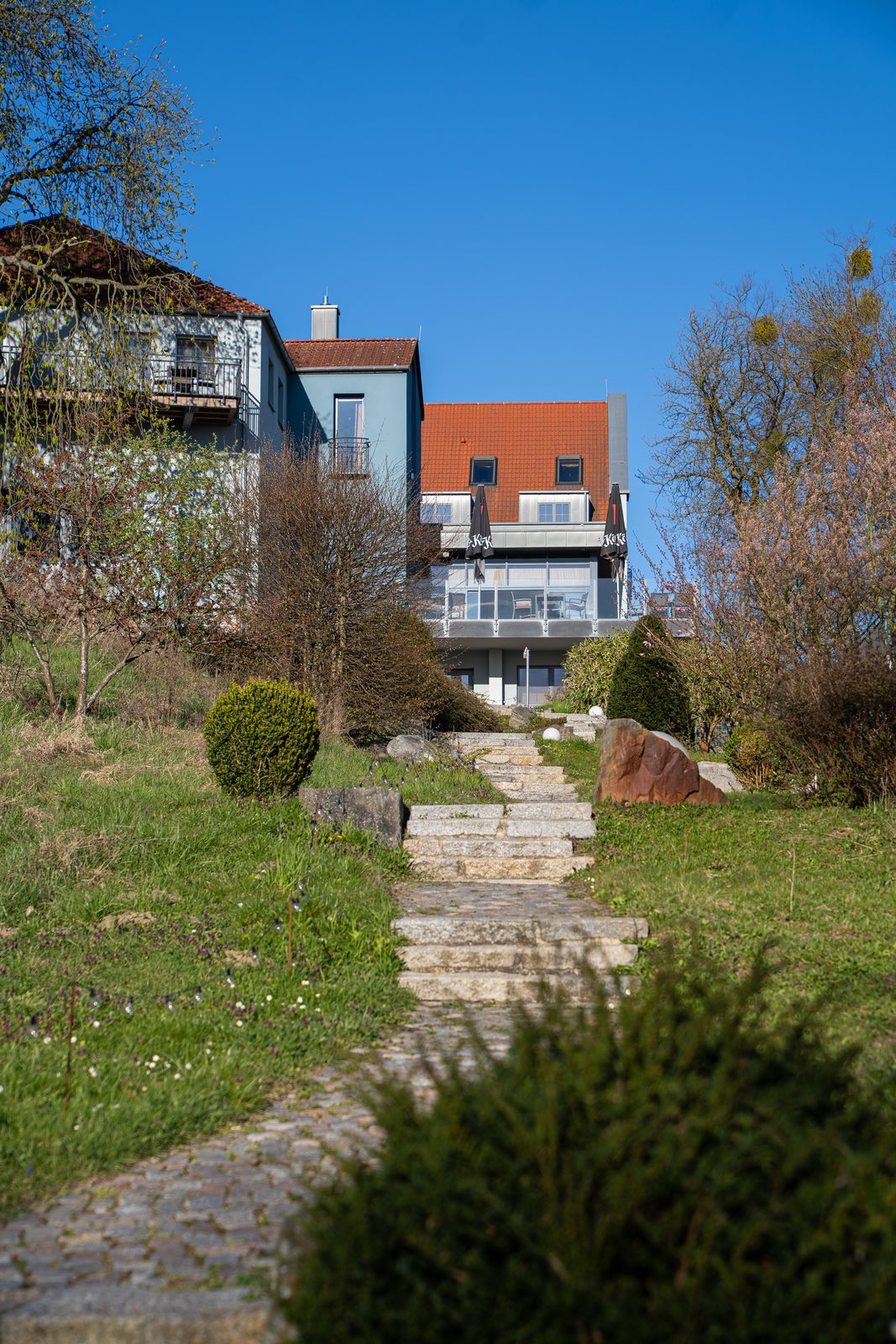 Steintreppe durch den Garten hinauf zum ArtHotel Kiebitzberg unter blauem Himmel