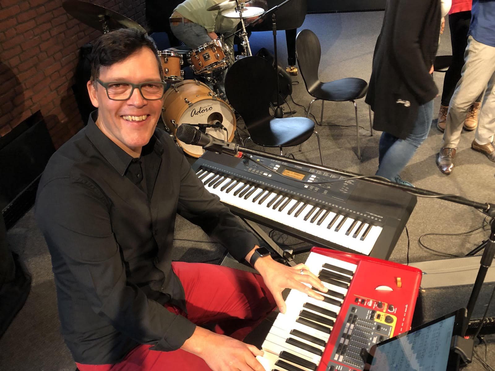 Frank Wedel lächelnd am Keyboard, im Hintergrund ein Schlagzeug