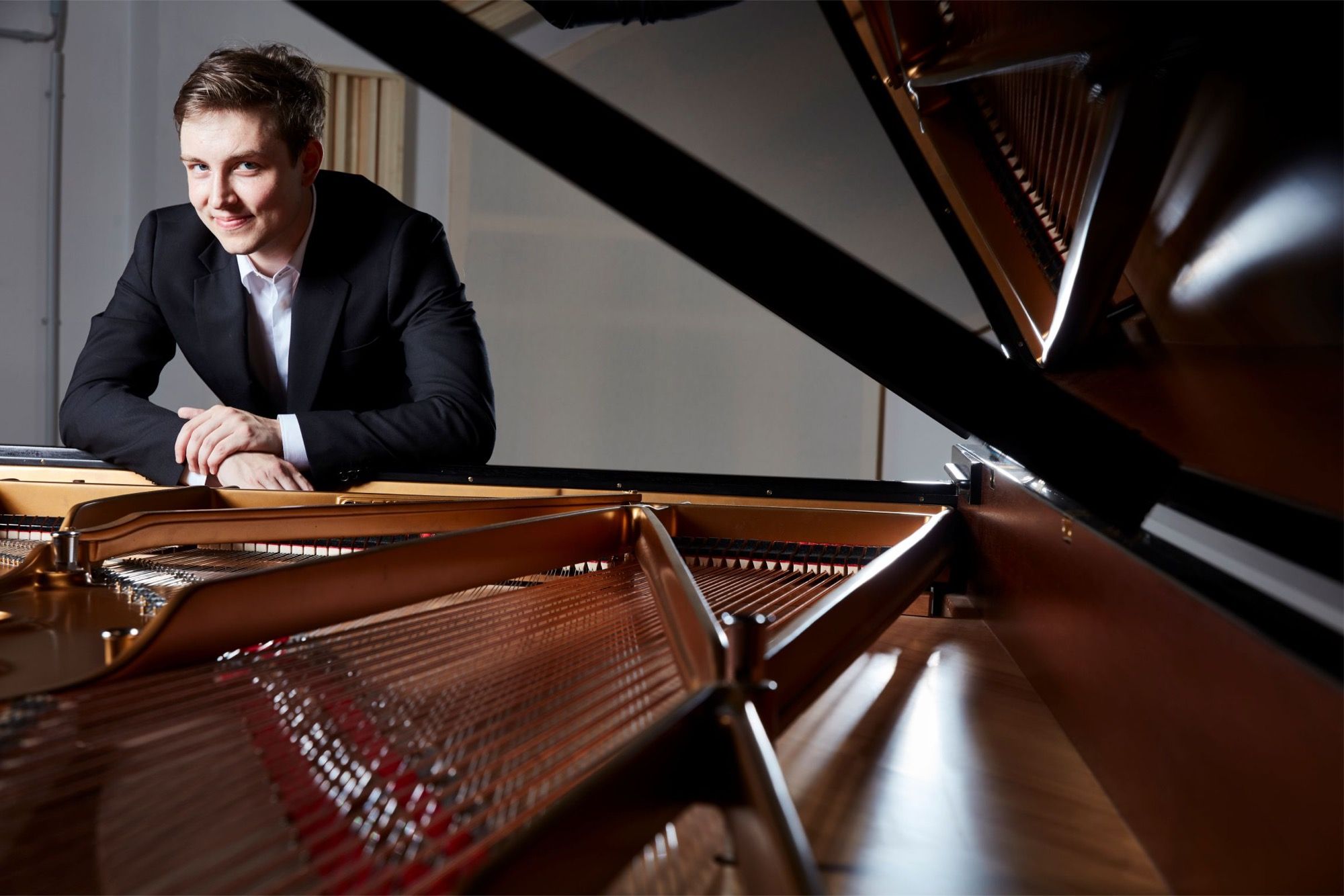 Pianist Florian Heinisch lächelnd hinter dem geöffneten Konzertflügel, Künstlerporträt zum Beethoven-Programm