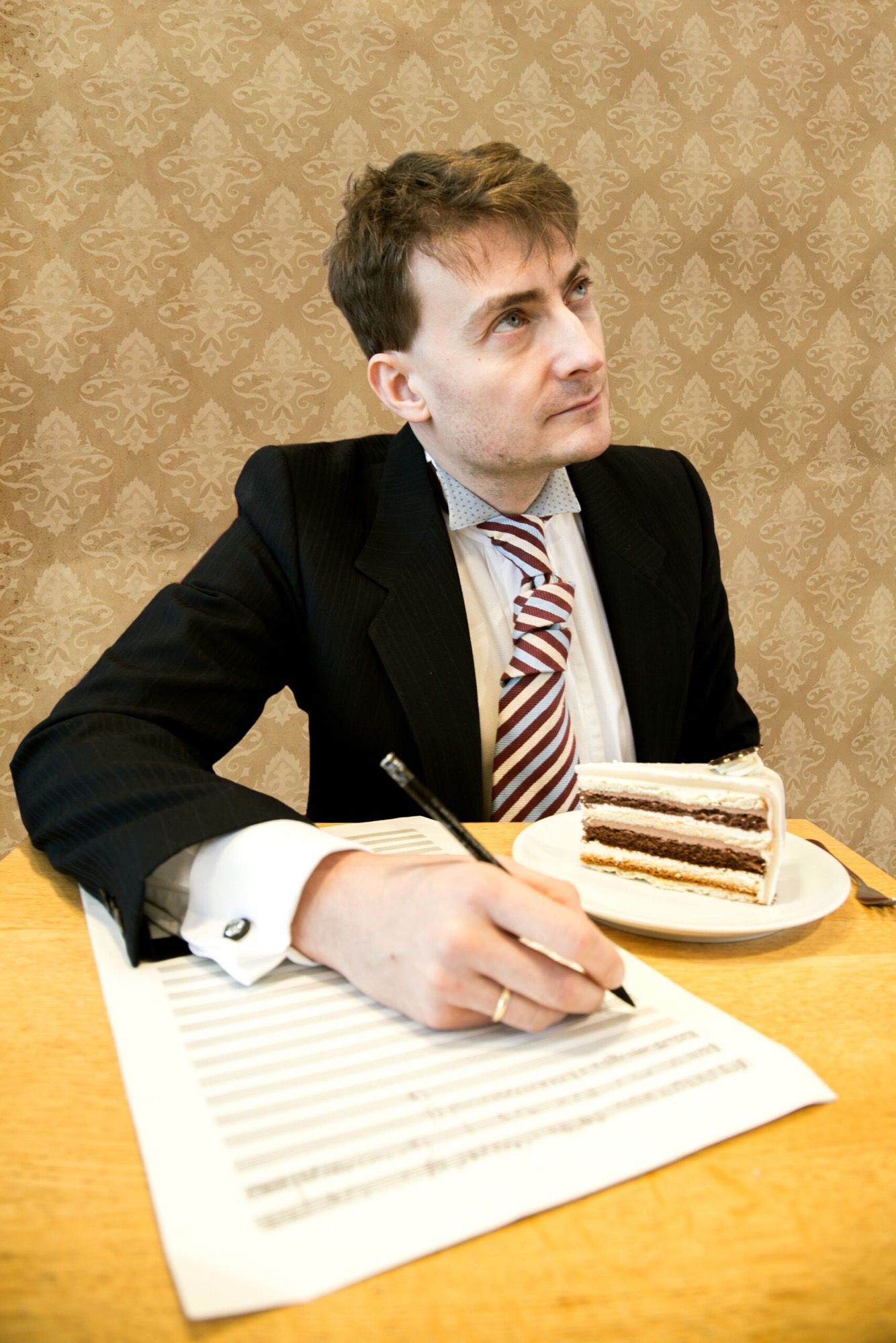 Liedermacher Sebastian Krämer im Anzug schreibt auf Notenpapier, daneben ein Stück Torte