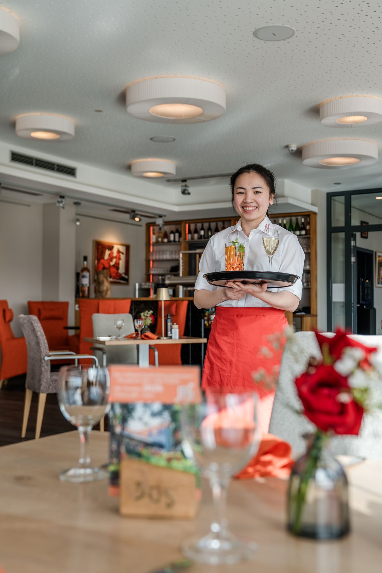 Lächelnde Servicekraft trägt Tablett mit Aperitif und Sekt durch das Restaurant des ArtHotel Kiebitzberg