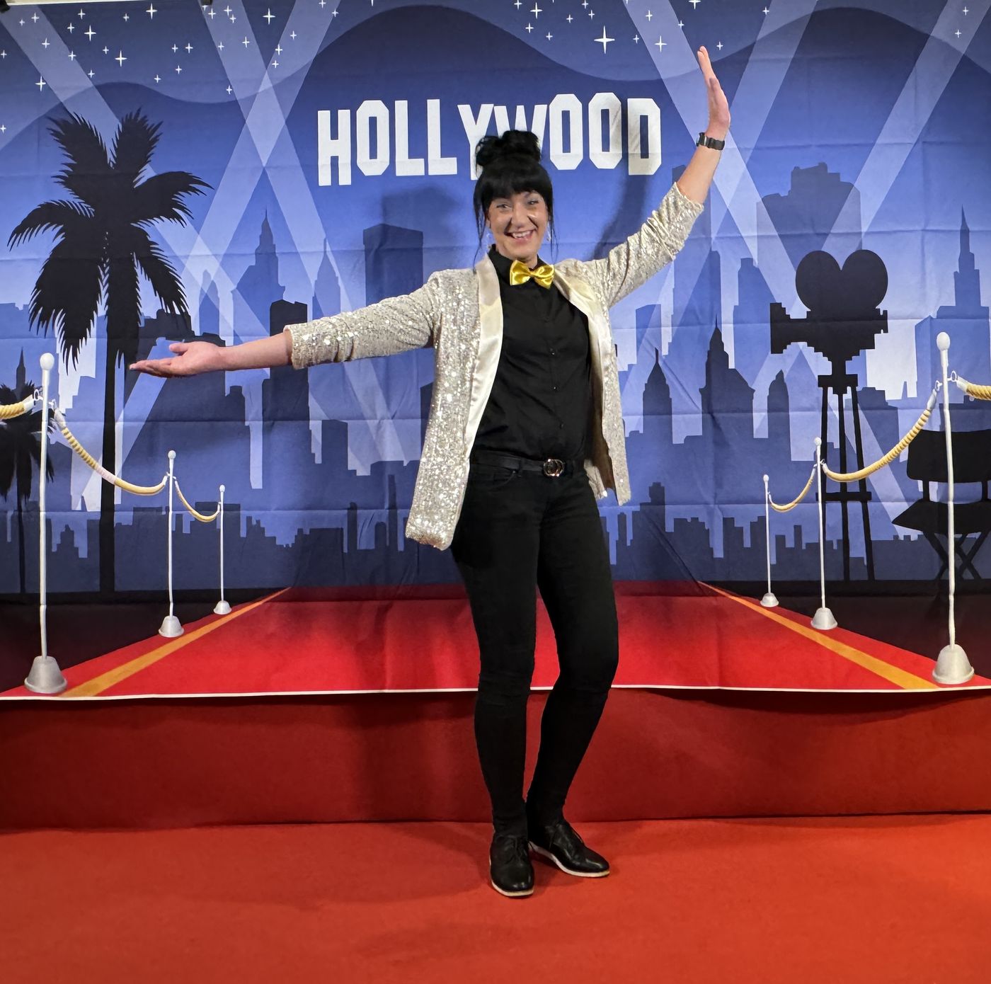 Guest in a glittering blazer with a golden bow tie posing on a red carpet in front of a Hollywood photo wall at ArtHotel Kiebitzberg