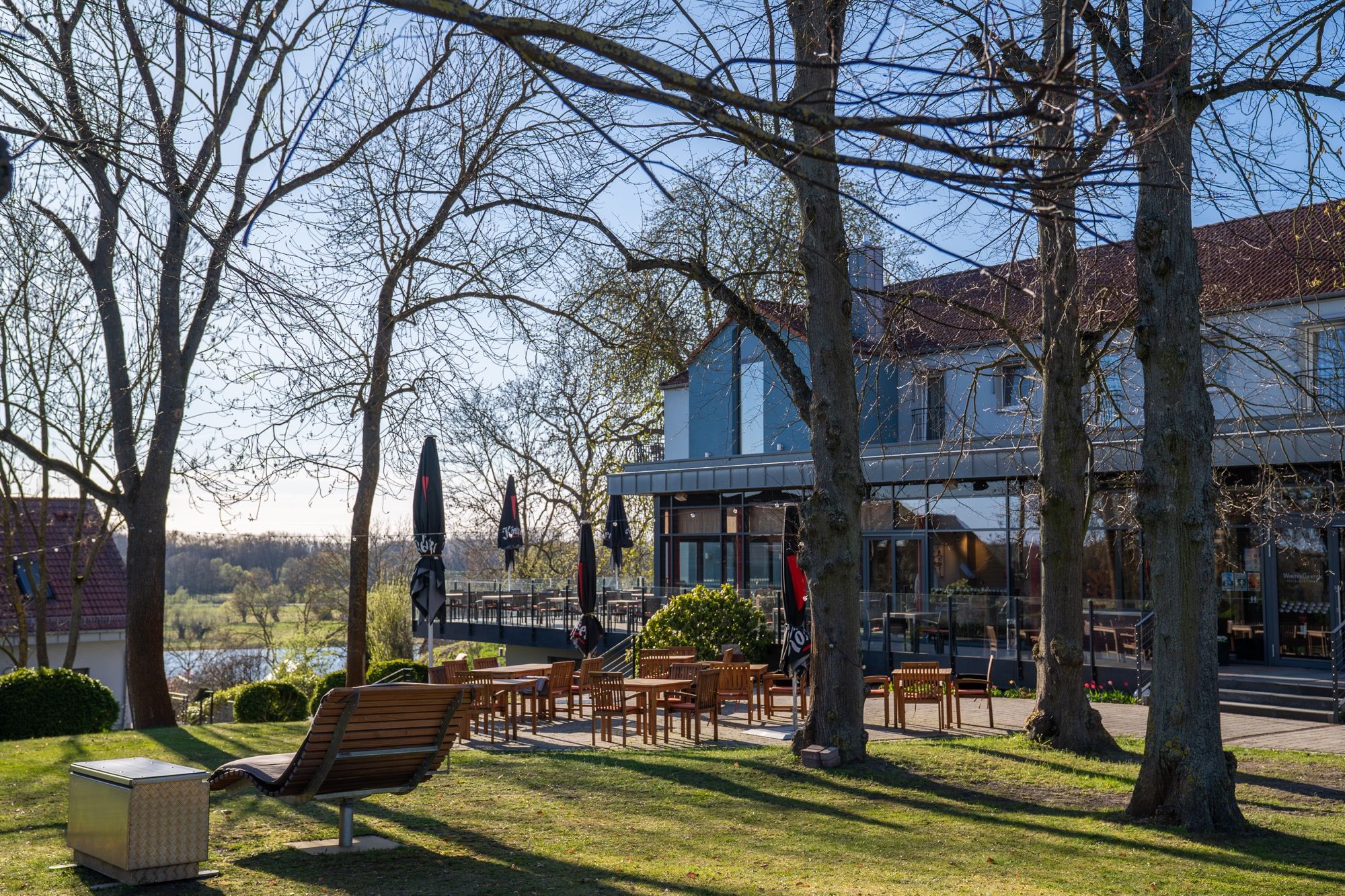 Parkanlage des ArtHotel Kiebitzberg im Frühling mit Bäumen, Liegen und Blick auf das Hotelgebäude und die Havel