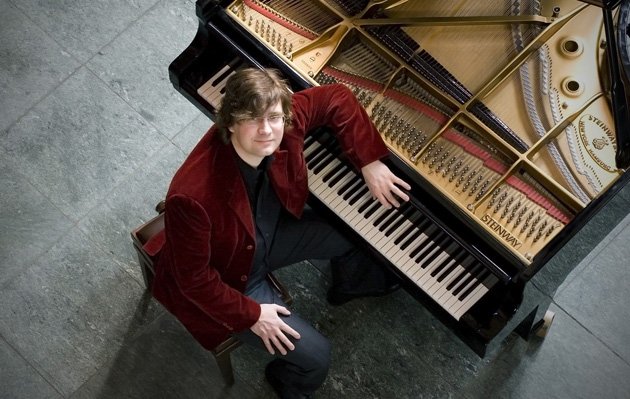 Pianist Stephan Graf von Bothmer in rotem Samtjackett kniet neben seinem Steinway-Flügel – Stummfilmkonzert im ArtHotel Kiebitzberg