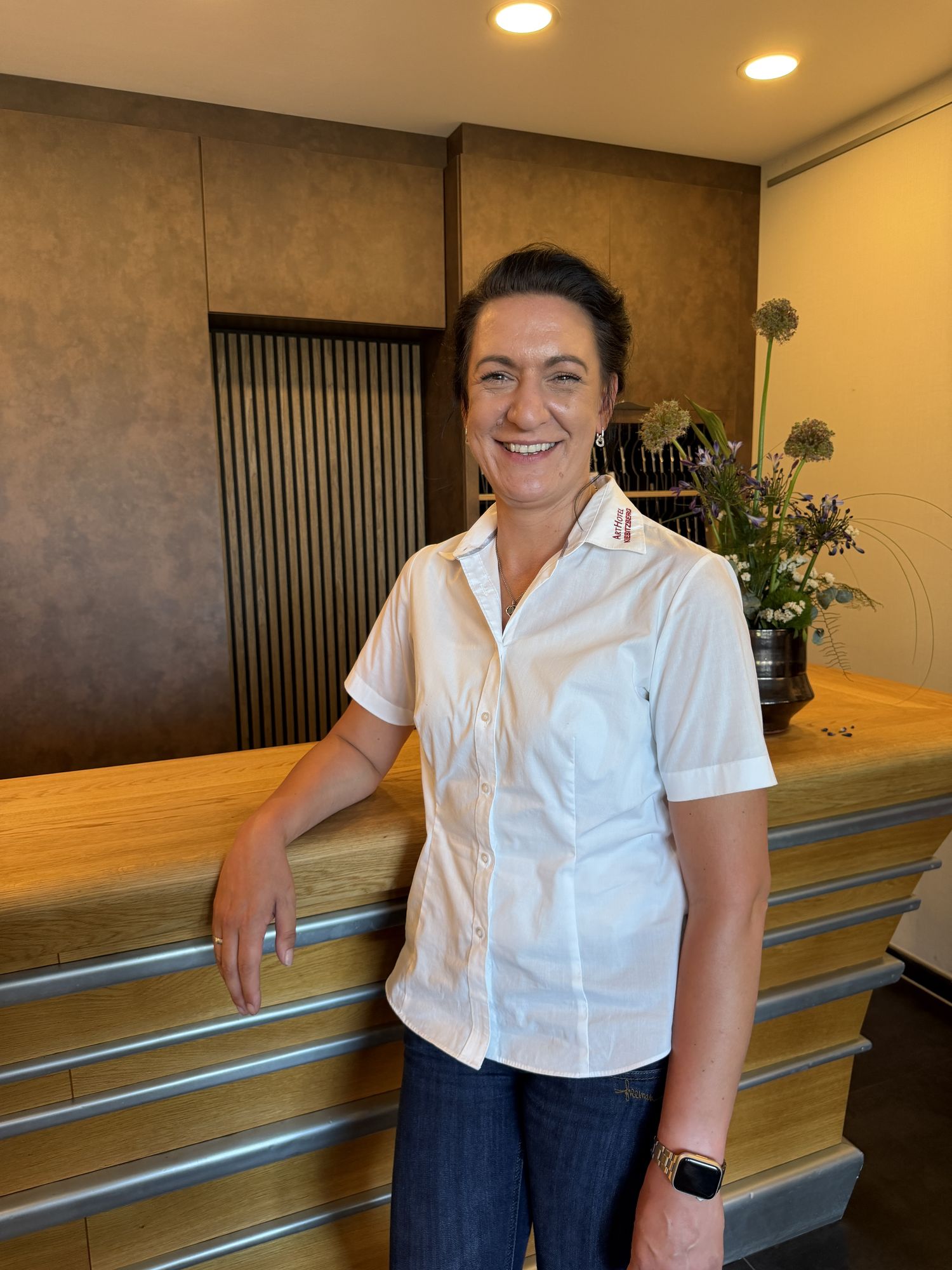 Smiling host Susi in an ArtHotel shirt at the wooden reception desk