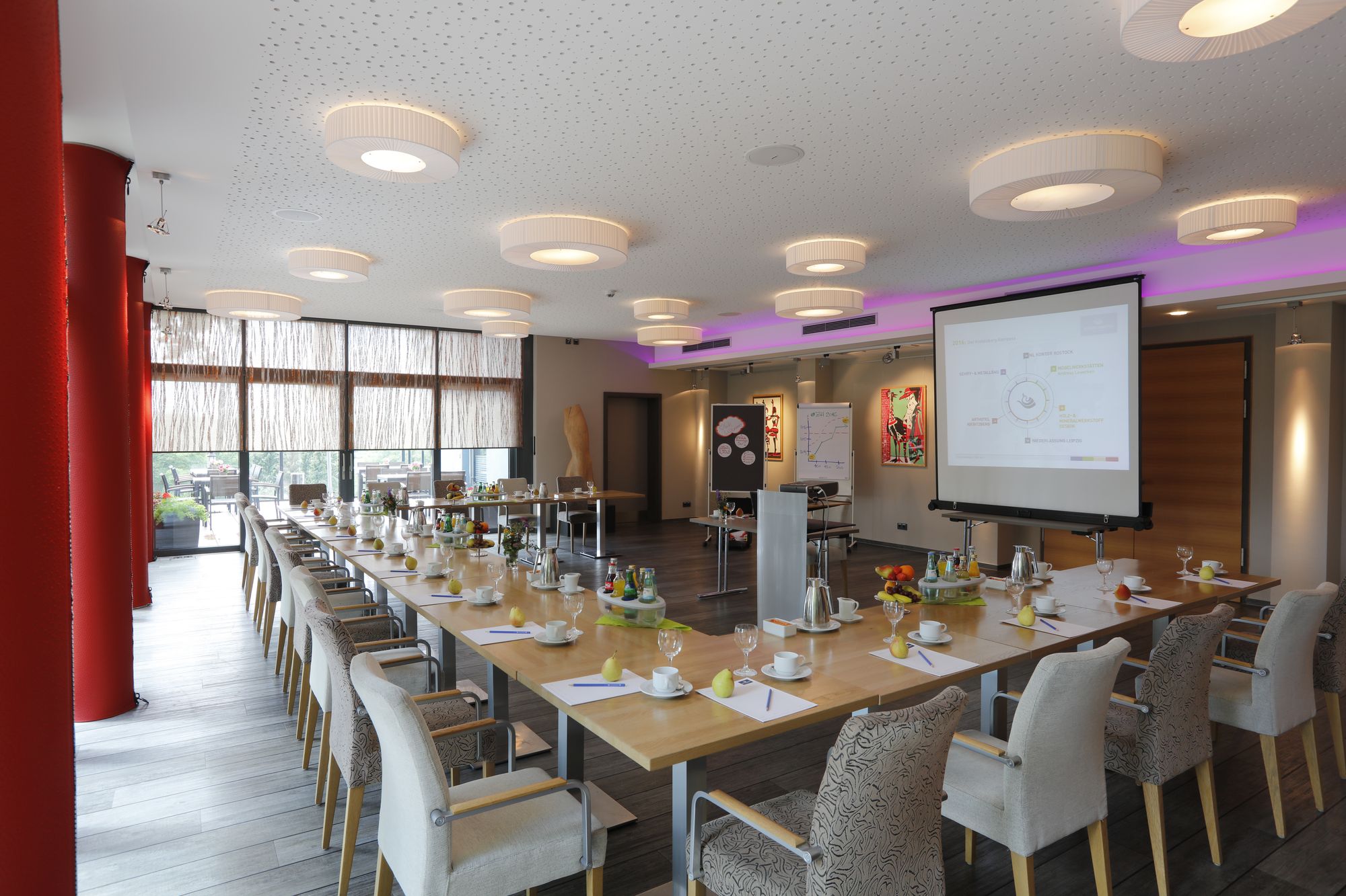 Festlich eingedeckter Tagungsraum im ArtHotel Kiebitzberg mit langer Tafel, Leinwand und Blick in den Garten