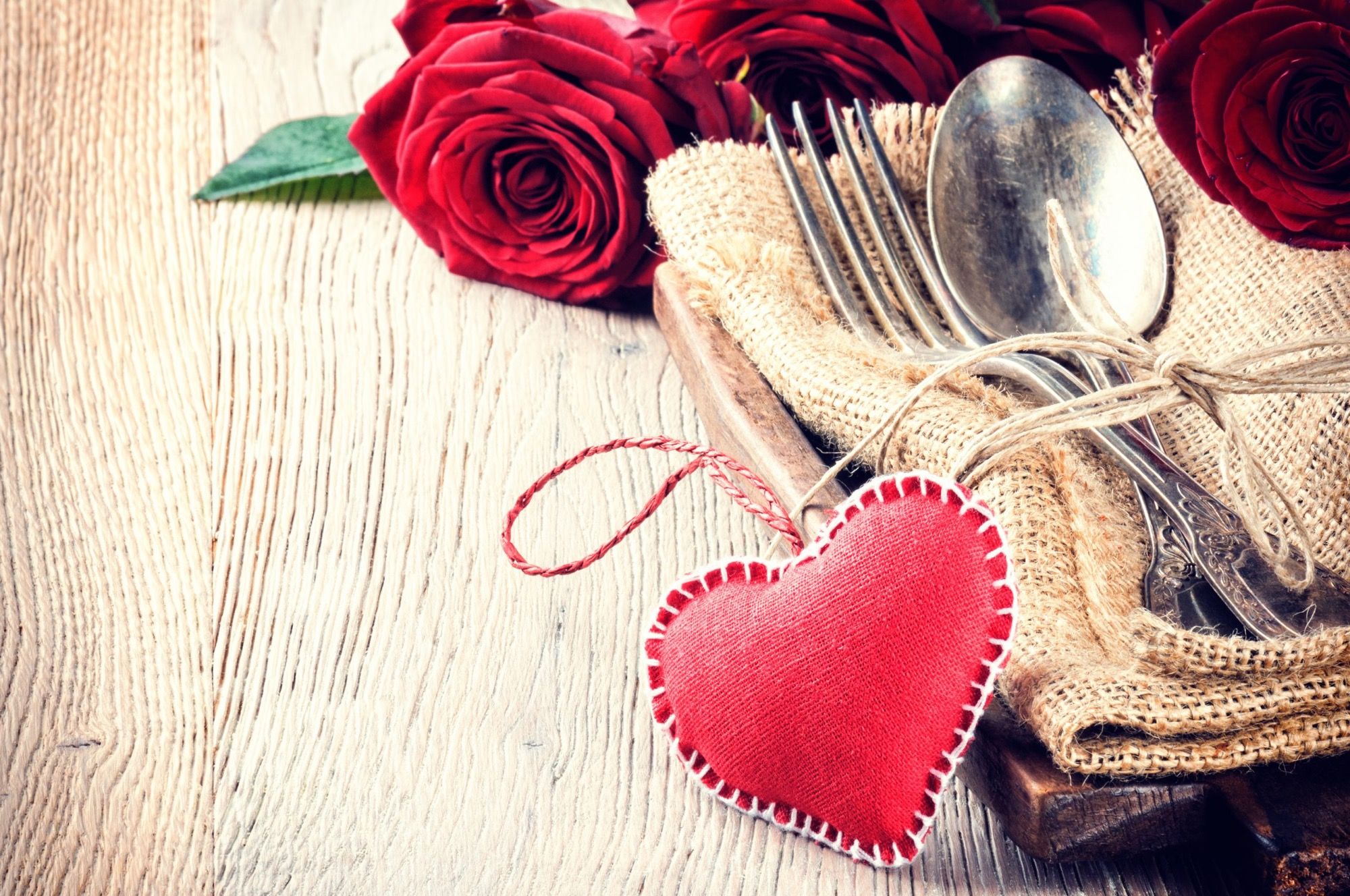 Rote Rosen, rotes Stoffherz und altes Besteck auf rustikalem Holztisch – Valentins-Candle-Light-Dinner im ArtHotel Kiebitzberg